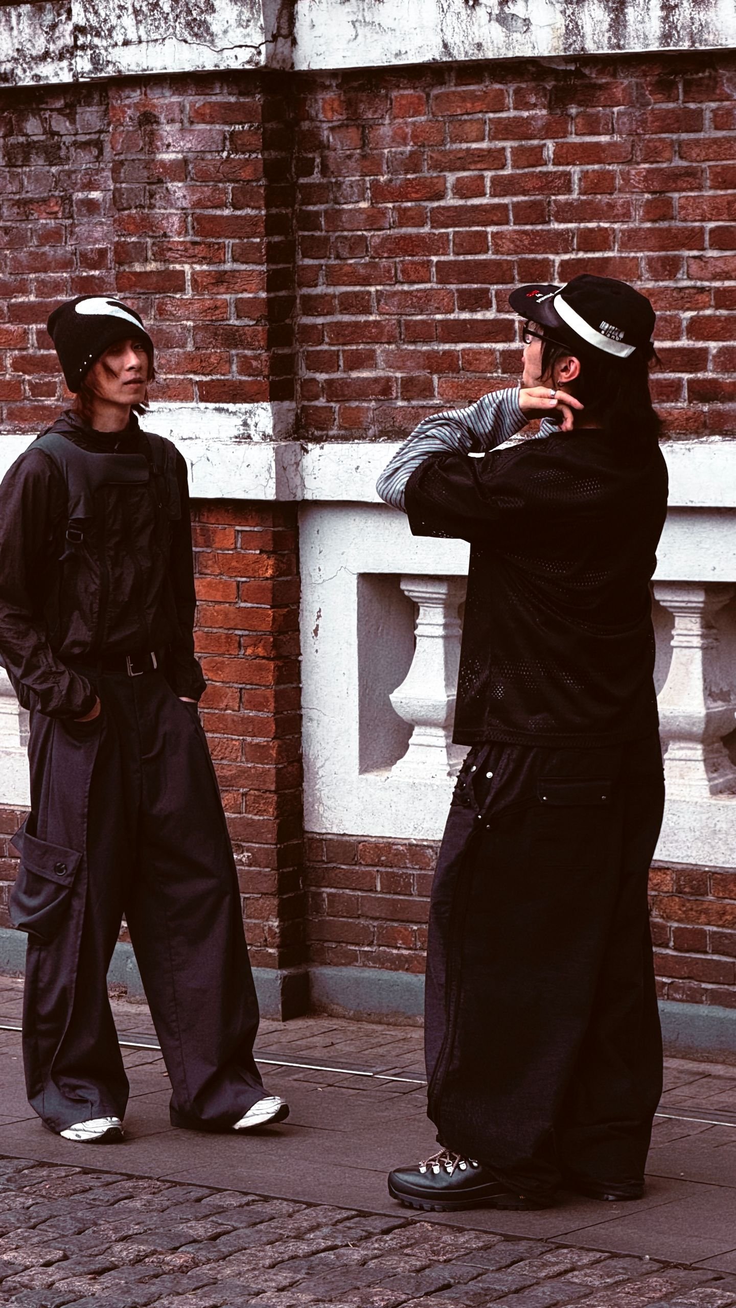Two stylish individuals in urban fashion pose against brick wall in Guangzhou, China.